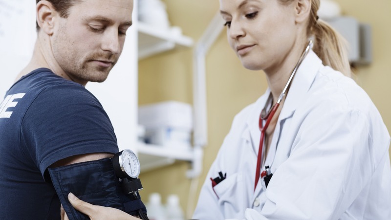 En kvinnlig läkare tar blodtryck på en man.