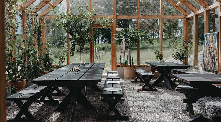 Bild inifrån ett växthus med bänkar och bord.