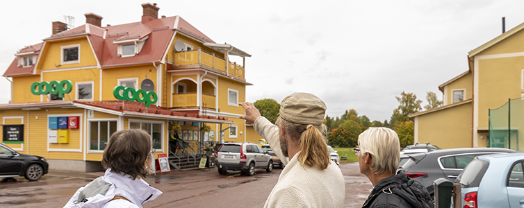 Tre personer med ryggen mot kameran pekar mot ett gult hus.