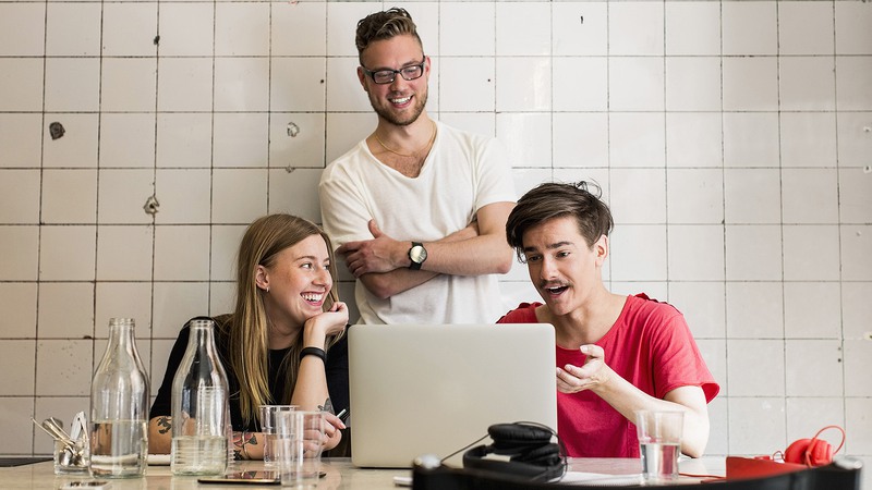 Tre personer ler och arbetar vid en dator.