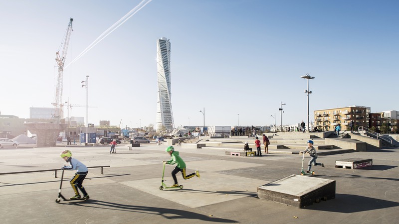 Barn åker sparkcykel i Malmö. Skyskrapan Turning torso syns i bakgrunden.