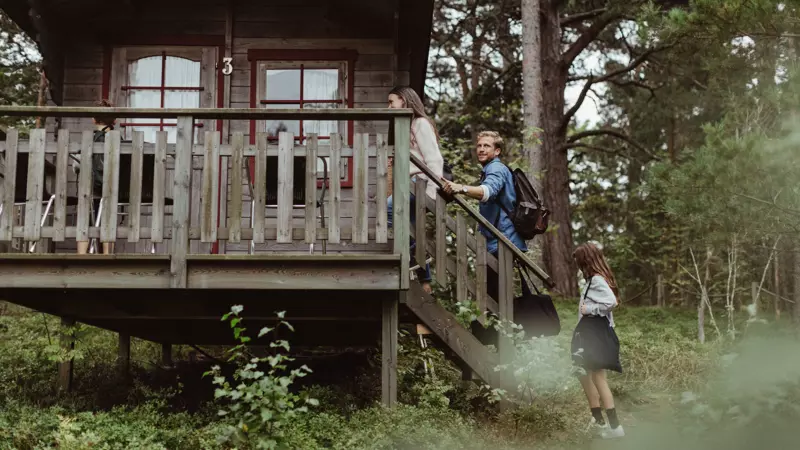 Tre turister går upp för utetrappa till hus i skogen.