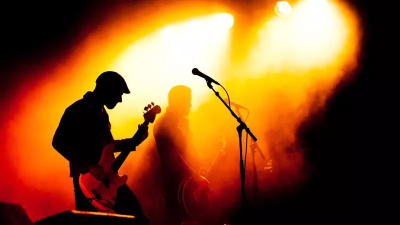 Musiker som spelar gitarr i mörk, men upplyst scenlokal.