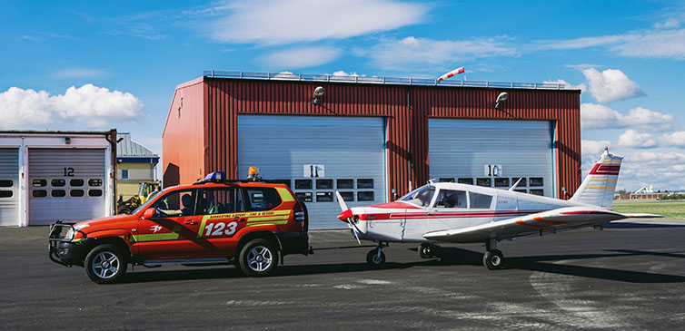 Flygplan och en röd bil framför hangar på landningsbana.