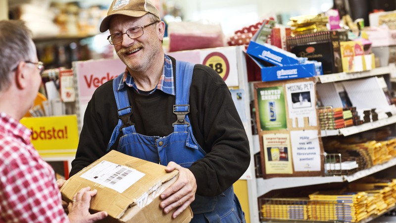 En man med keps och glasögon hämtar ut ett postpaket i en matvarubutik.