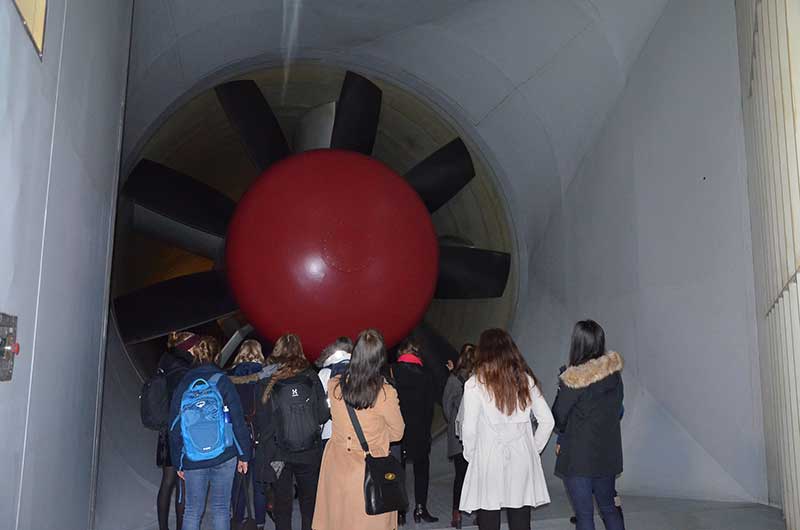 Flera tjejer står i en tunnel och kollar på en stor fläkt