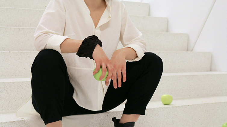 Kvinna i vit blus sitter i en trappa med ett grönt äpple i handen.