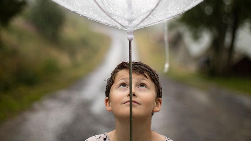 Pojke som håller i ett paraply och blickar upp mot paraplyet