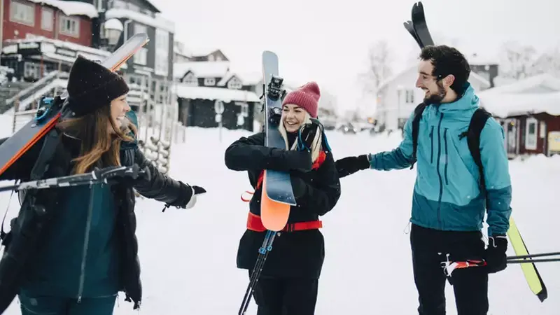 Två kvinnor och en man bär på skidor. 